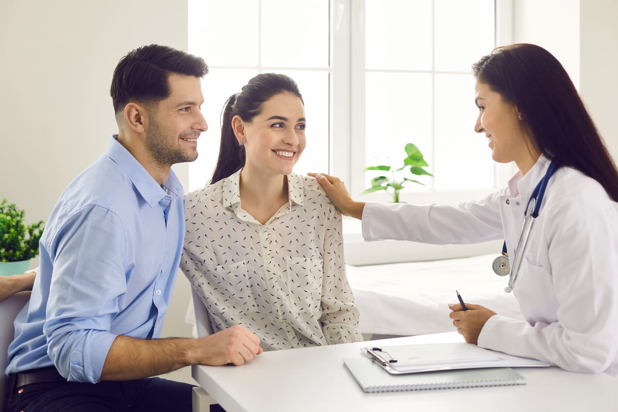 Young couple having initial fertility consultation with female doctor in bright clinic office, discussing when to start IVF and fertility treatment options