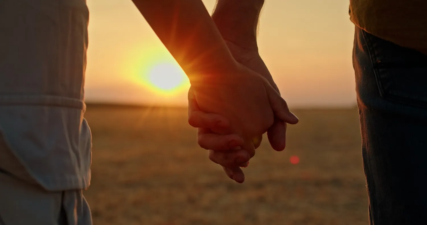 Gros plan sur un couple se tenant la main au coucher du soleil, dans un champ paisible. L’image illustre le soutien émotionnel, la connexion et la force partagée dont de nombreux couples font preuve lorsqu’ils se préparent à leur premier cycle de FIV.