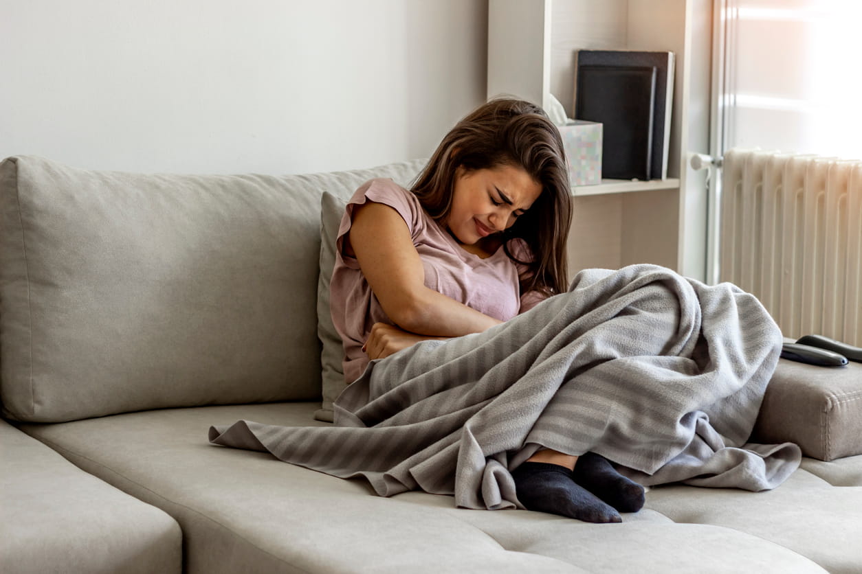 Vrouw met menstruatiepijn op de bank, ter illustratie van waarschuwingssignalen zoals ernstige dysmenorroe en menstruele onregelmatigheden die een vroeger vruchtbaarheidsconsult rechtvaardigen